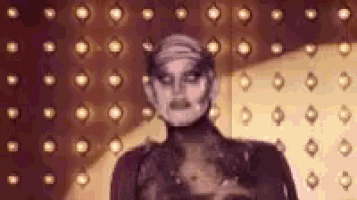 a woman with a mask on her face is standing in front of a wall with lights on it .