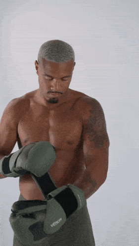 a man without a shirt is putting on boxing gloves that say venum