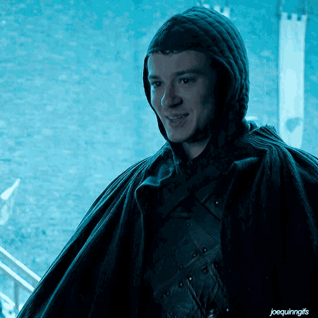 a man wearing a black cape with a hood is smiling in front of a castle banner