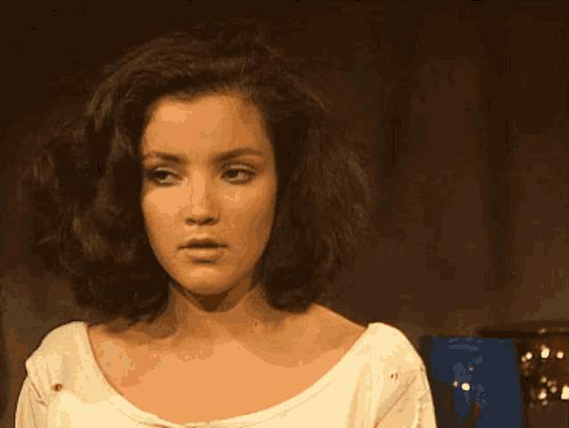 a woman with brown hair and a white shirt is looking at the camera
