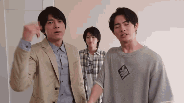 a man wearing a gray shirt with the letter s on it stands between two other men