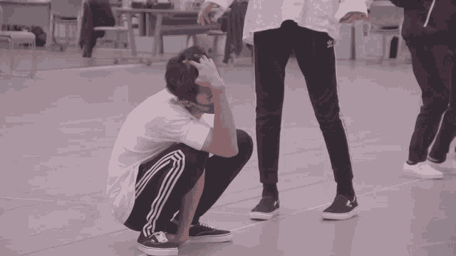 a man squatting down with his head in his hands and a woman standing behind him wearing adidas pants