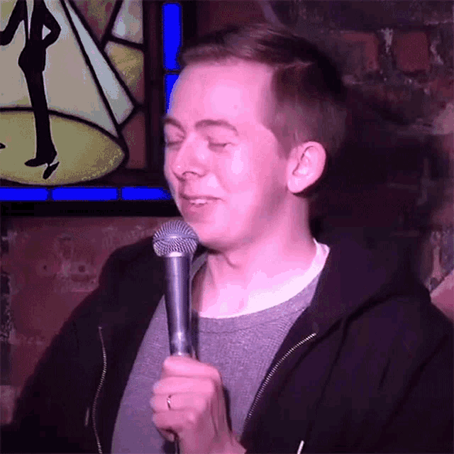 a man with a ring on his finger is holding a microphone in front of a stained glass window