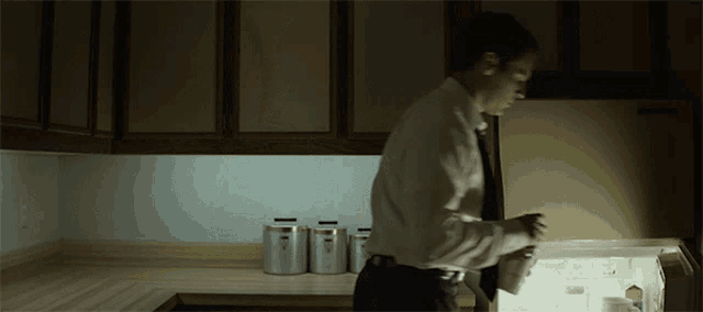 a man in a white shirt is opening a refrigerator in a kitchen