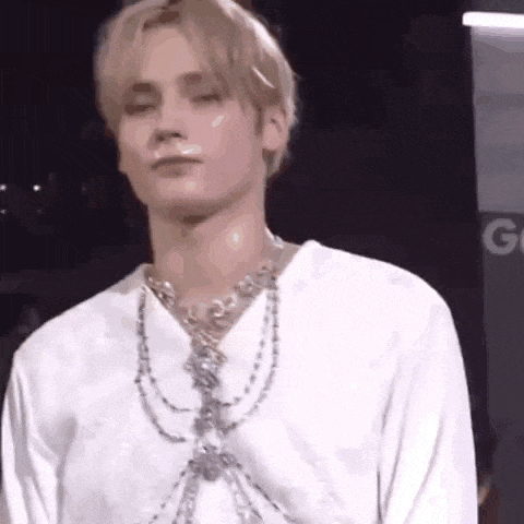 a man wearing a white shirt and a necklace is standing on a stage .