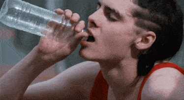 a man in a red tank top drinks water from a clear plastic bottle