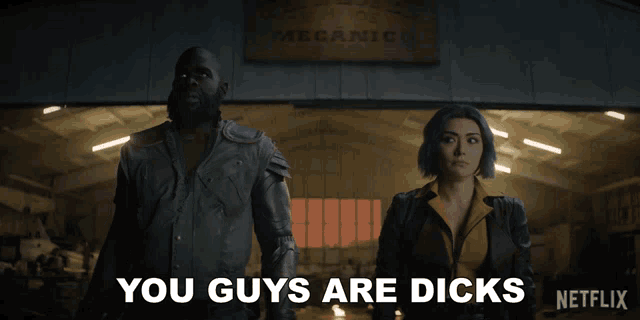 a man and woman are standing in front of a sign that says you guys are dicks