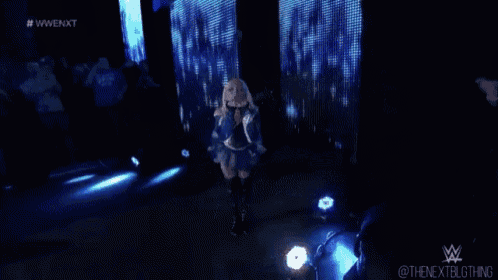 a woman in a blue dress is standing on a stage in front of a crowd in a dark room .