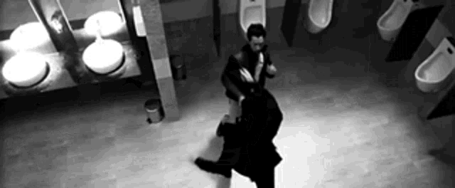 a black and white photo of a man holding another man in a public restroom .