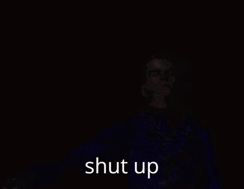 a man in a blue jacket is holding a gun with the words shut up below him .