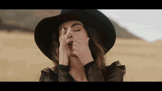 a woman in a black hat is covering her nose with her hand