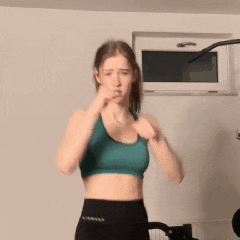 a woman in a green sports bra and black pants is standing in front of a window .