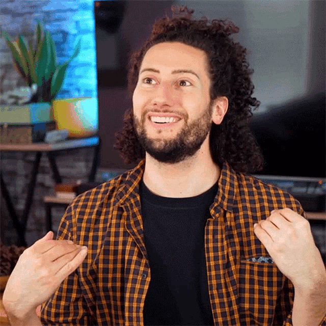 a man with curly hair and a beard wearing a plaid shirt is smiling