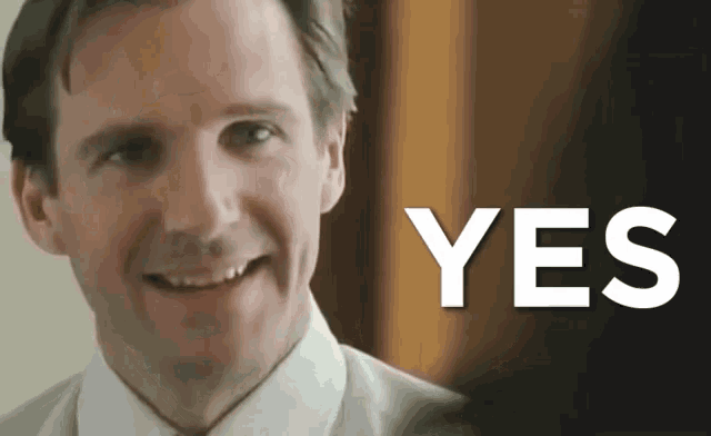 a man in a suit and tie smiles in front of a yes sign