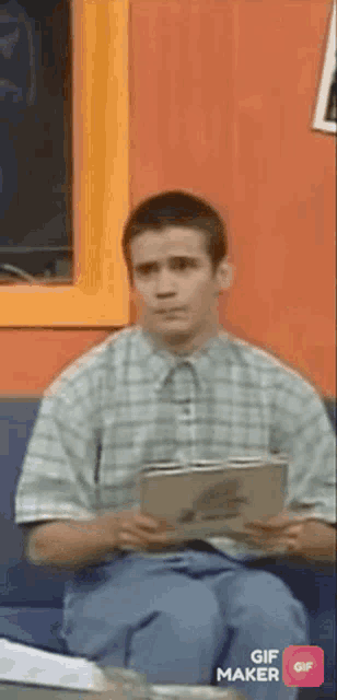 a young man is sitting on a couch holding a book .