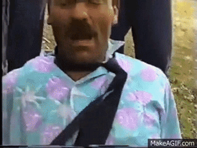 a man with a mustache is wearing a tie and a shirt with flowers on it .