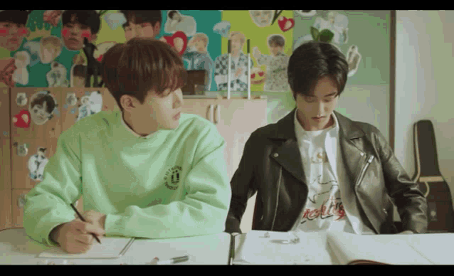 two young men are sitting at a table with one wearing a green sweater that says ' u. ' on it