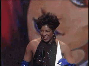 a woman in a black dress and blue gloves is holding a trophy in front of a microphone