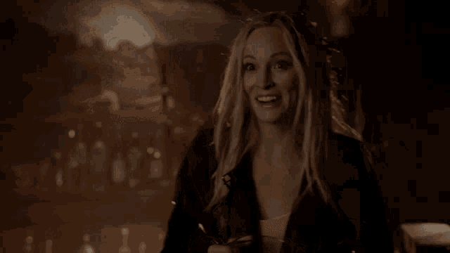 a woman in a black jacket is smiling and holding a glass of wine