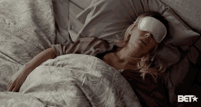 a woman is sleeping in a bed with a sleep mask on her eyes