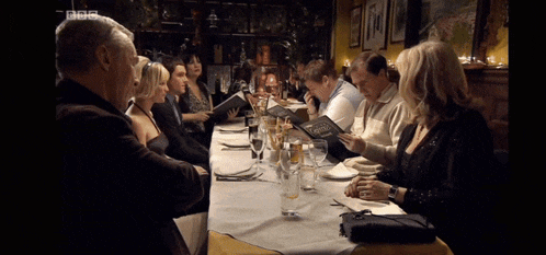 a group of people sitting at a long table with bbc written on the bottom left