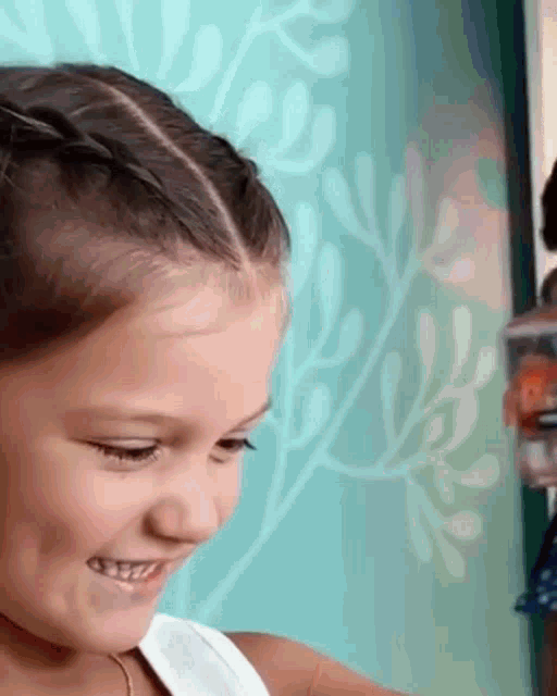 a little girl with braids in her hair is smiling in front of a green wall .