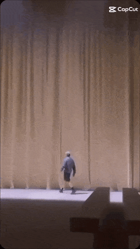 a man is walking in front of a curtain with the caption capcut on the bottom