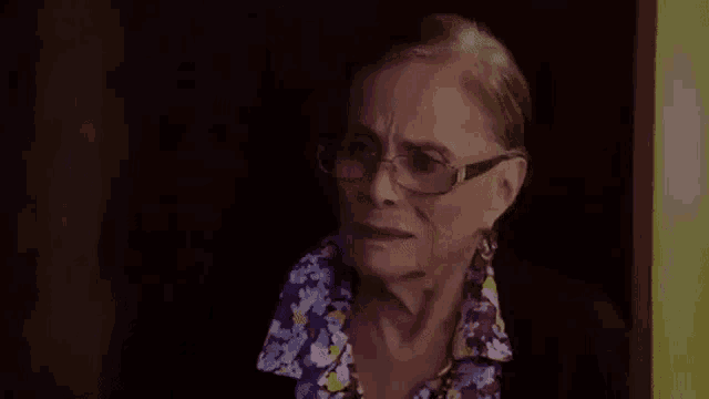 an elderly woman wearing glasses is standing in a dark room .