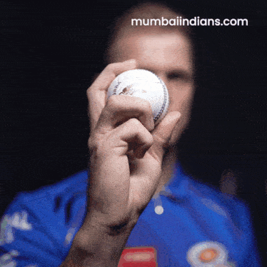 a man in a blue shirt is holding a cricket ball in his hand