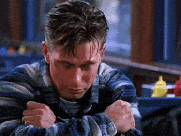 a man in a plaid shirt is hugging his arms and looking down