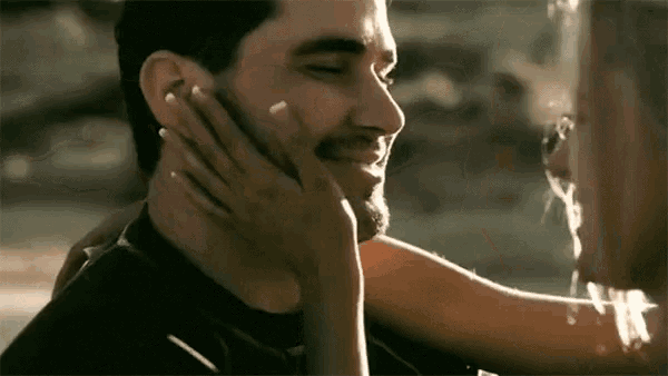 a woman is touching a man 's face with her hand while he is smiling .