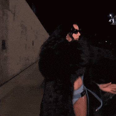 a woman wearing sunglasses and a fur coat is walking down the street at night
