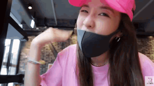 a woman wearing a pink shirt and a pink hat is wearing a black face mask