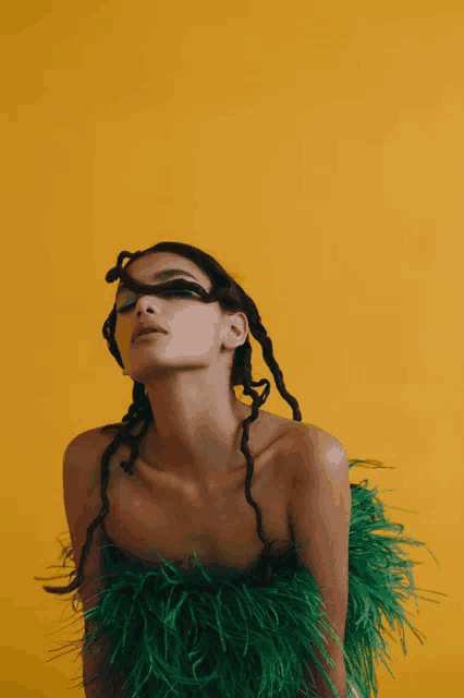 a woman is wearing a green feathered top and a yellow background