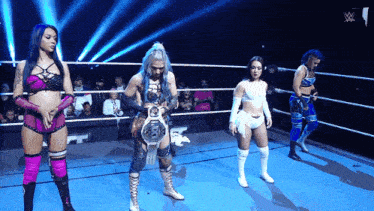 a group of women are standing in a wrestling ring and one of them is holding a championship