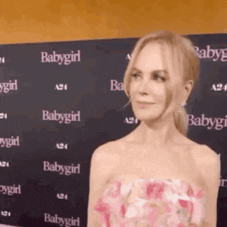 a woman in a pink dress is standing in front of a wall that says babygirl on it .