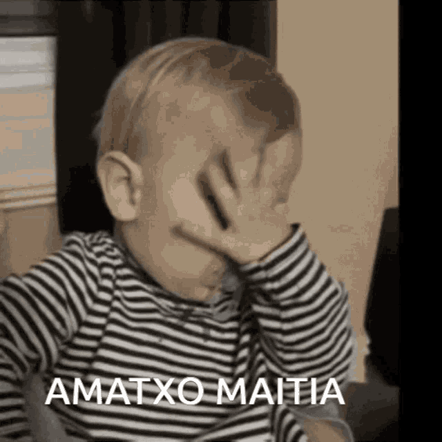 a baby in a striped shirt covering his face with his hand and the words amatxo maitia above him