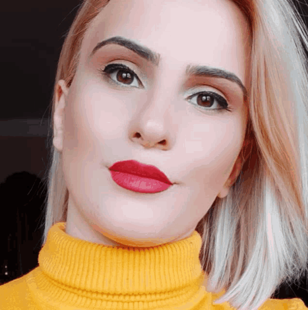 a woman wearing a yellow turtleneck and red lipstick looks at the camera