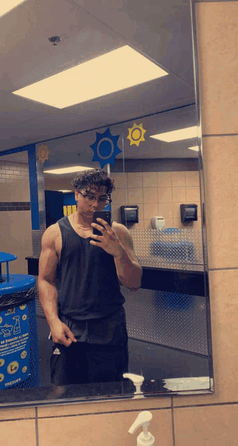 a man taking a selfie in a bathroom with a trash can that says ' recycle ' on it