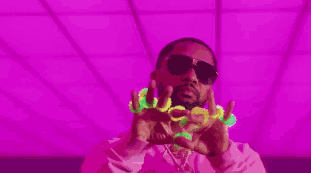 a man wearing sunglasses and a pink shirt is holding glow in the dark objects