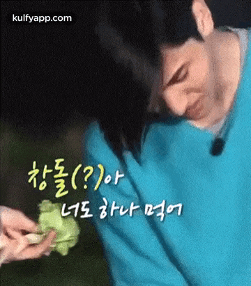 a man in a blue sweater is holding a piece of lettuce in his hands .