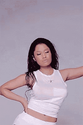 a woman in a white tank top and white shorts is standing with her hands on her hips .