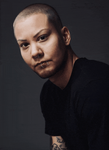 a man with a tattoo on his arm is wearing a black shirt and looking at the camera