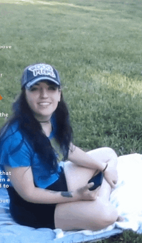 a woman wearing a hat that says ' snoop dogg ' on it sits on a blanket in the grass