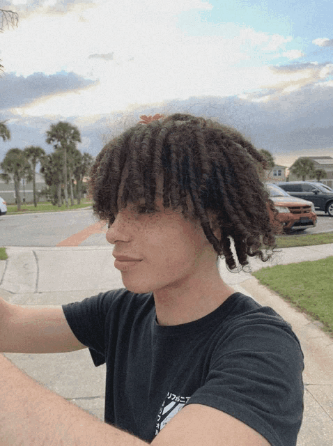 a young man with curly hair is wearing a black t-shirt with a japanese symbol on the front