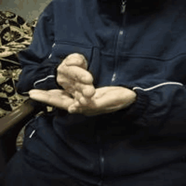 a person wearing a blue jacket is sitting in a chair with their hands folded .
