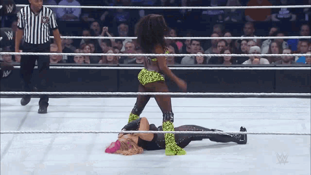 two women are wrestling in a wrestling ring with a referee in the background