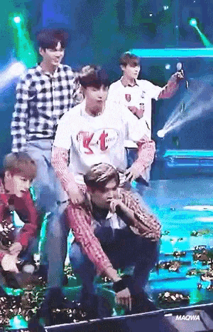 a group of young men are performing on a stage and one of them is kneeling down while holding a microphone .