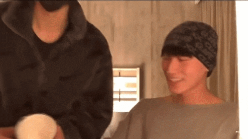two men are standing next to each other in a room and one of them is wearing a hat .