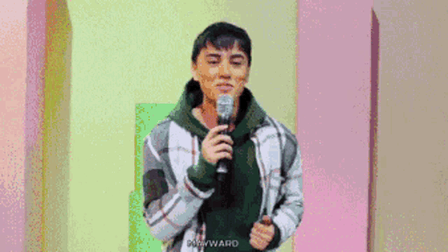 a man in a plaid jacket is holding a microphone and the word mayward is on the bottom right
